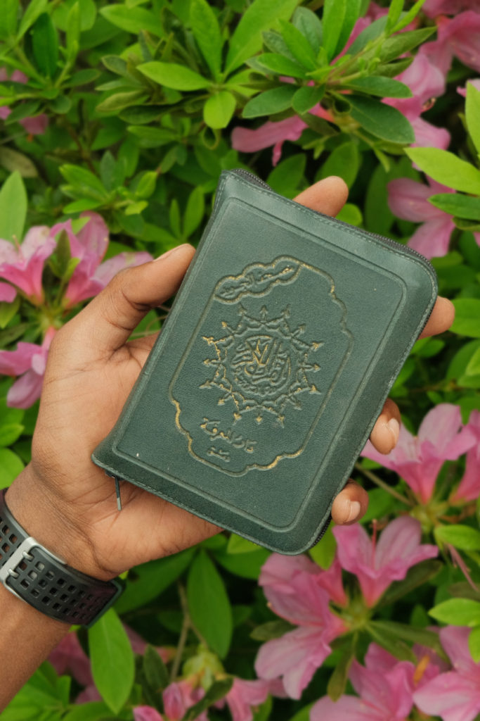 A hand holding the Qur'an on a backgdrop of flowers.